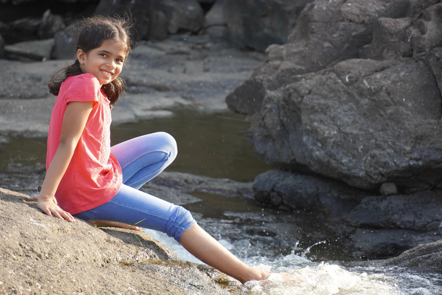 A picture of Shruti sitting on rocks on the banks of a stream.